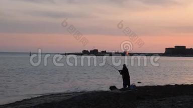 粉红色日落时人们在海上投掷鱼竿的剪影。 日落时分，渔民在海滨捕鱼